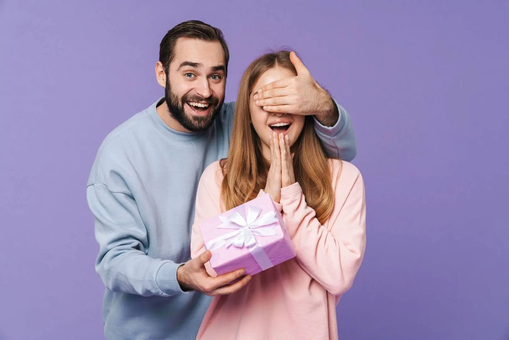 happy young man covering eyes his girlfriend isolated purple wall holding gift box wp jpg