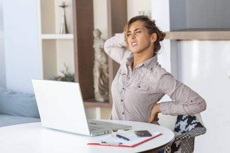 portrait young stressed woman sitting home office desk front laptop touching aching back with pained expression suffering from backache after working laptop wp